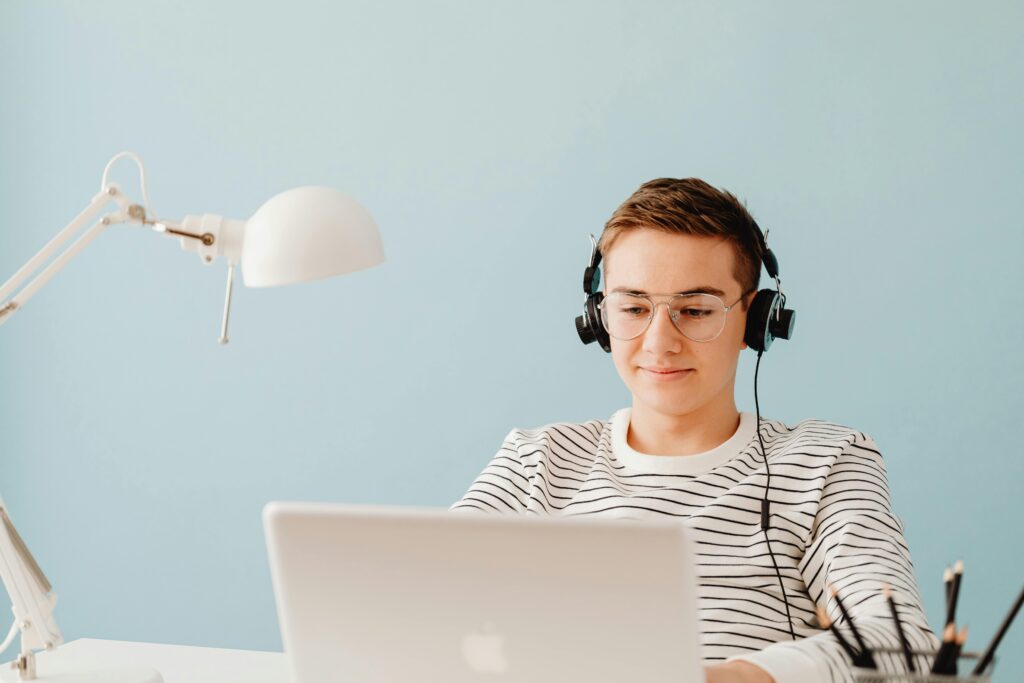 Teenager with headphones working on laptop in home office, exemplifying remote learning.